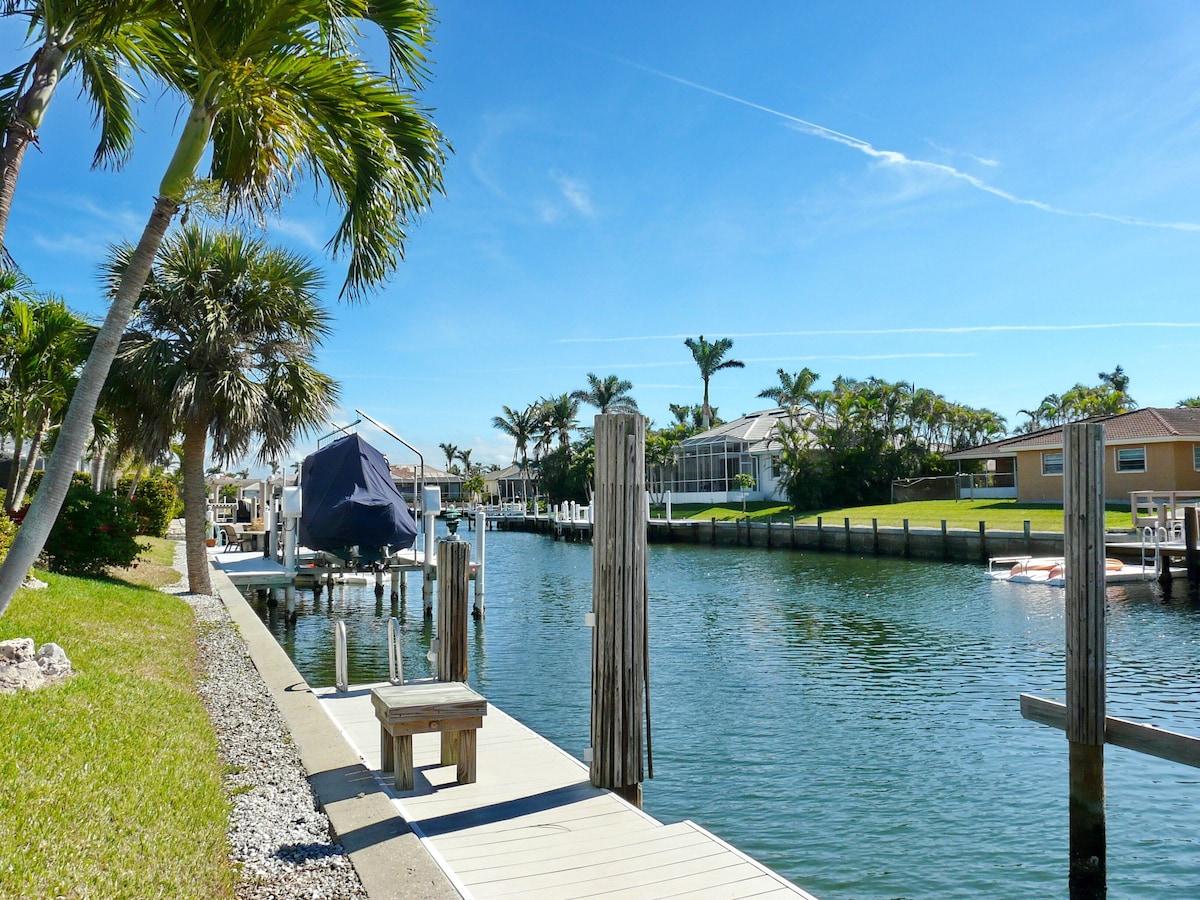 A waterfront dock with a covered seating area, a wooden bench, and a small boat.