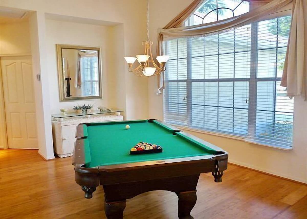 A pool table in a room with a large window, a mirror, and a chandelier.