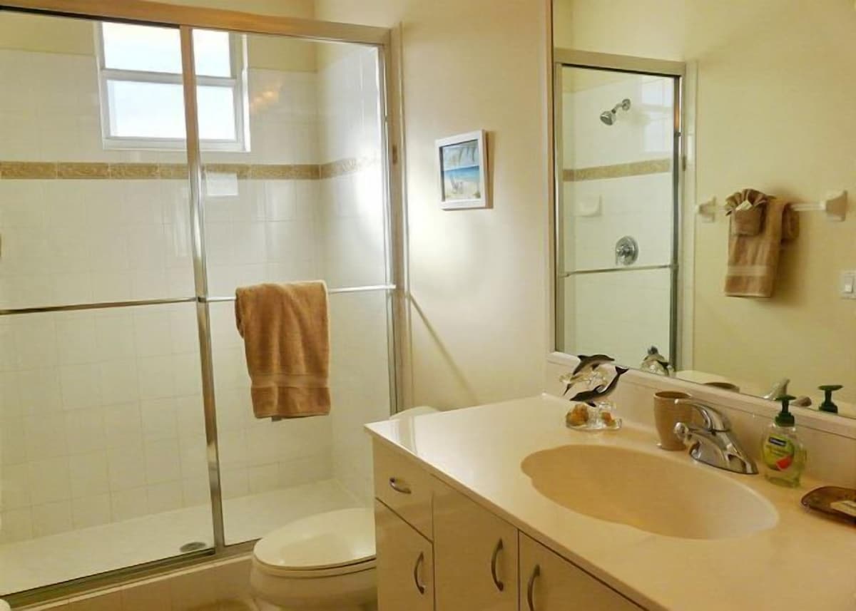 A bathroom with a glass shower enclosure, a toilet, a sink with a mirror, and a towel hanging on the wall.