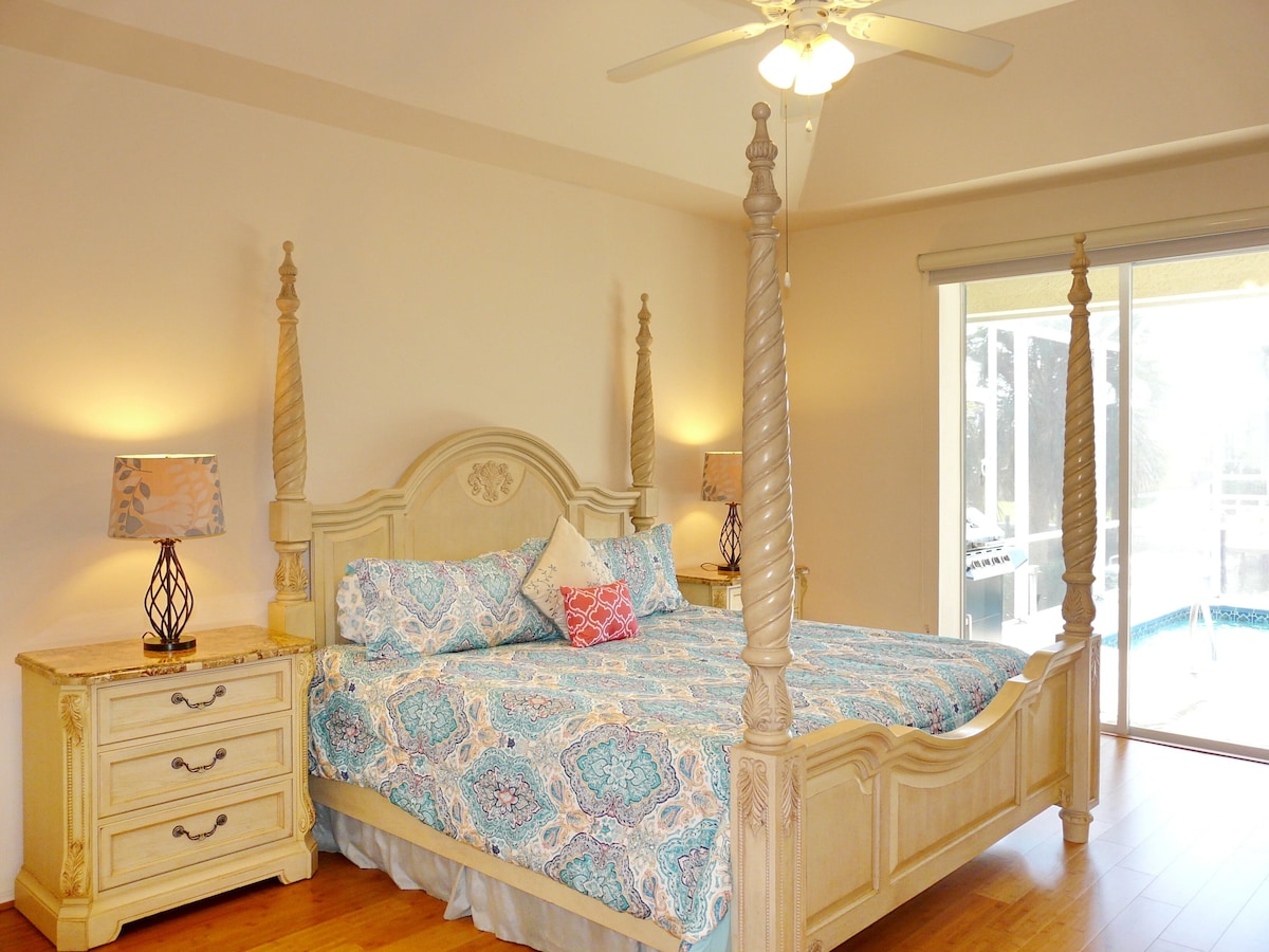 A four-poster bed with a canopy, a bedside table with drawers, and a lamp.
