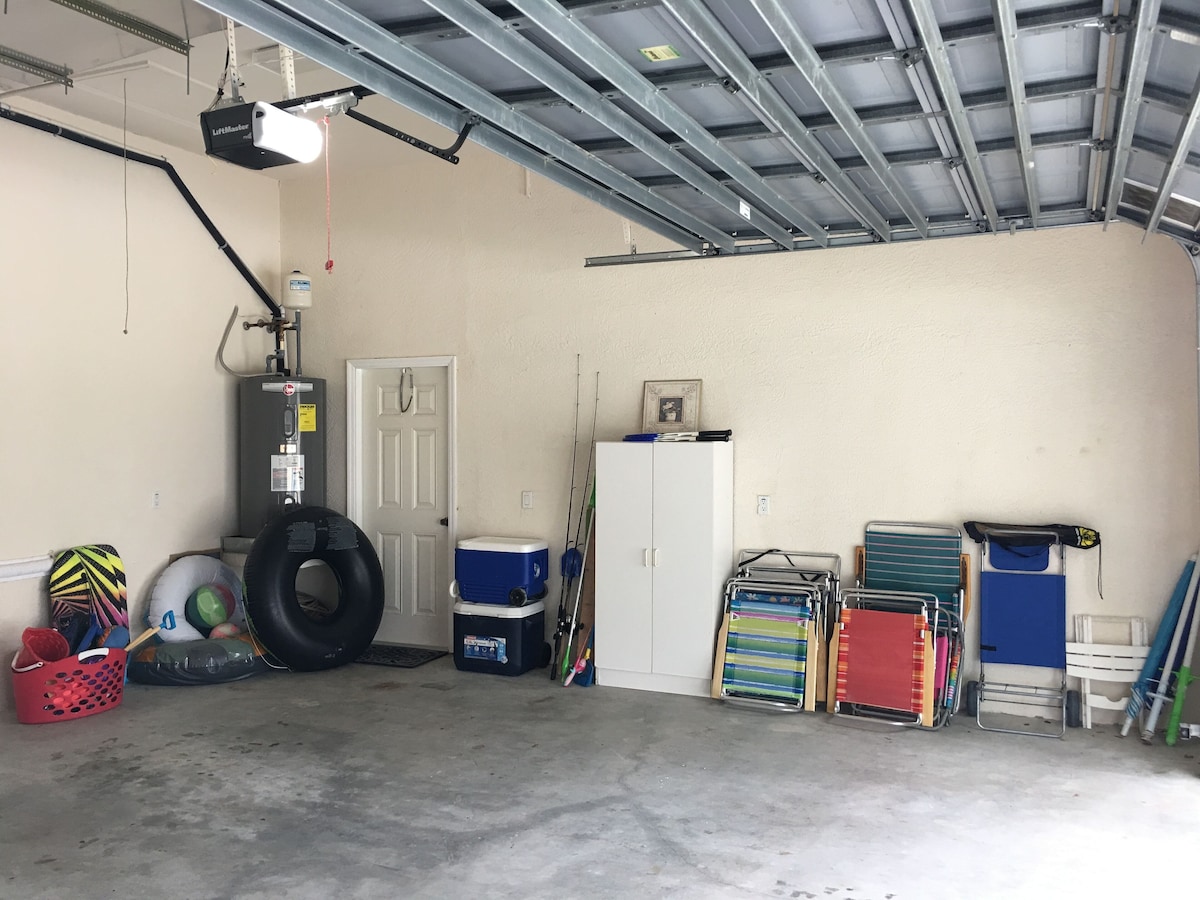 A garage with a ceiling fan, a water heater, a door, and various storage items like a cooler, shelves, and a tire.