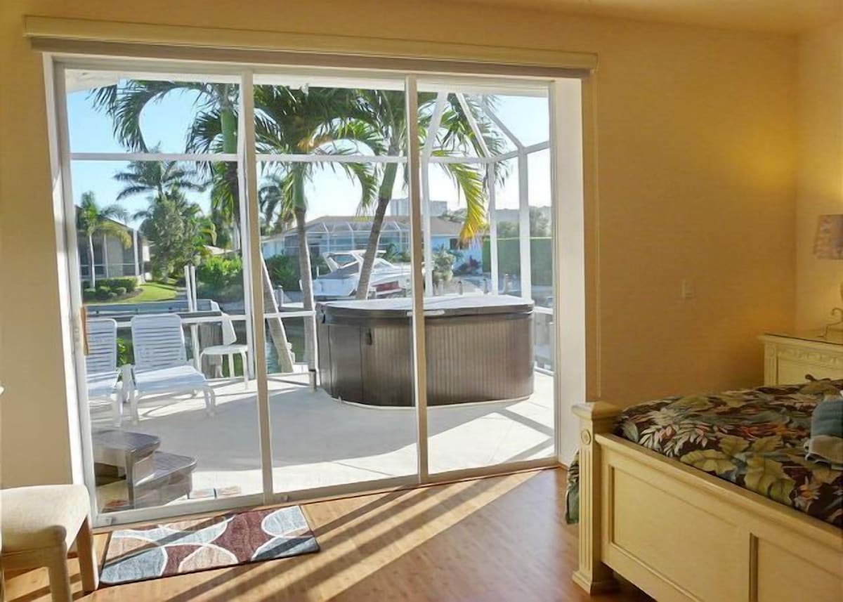 A room with a sliding glass door leading to a balcony with a hot tub and outdoor seating.