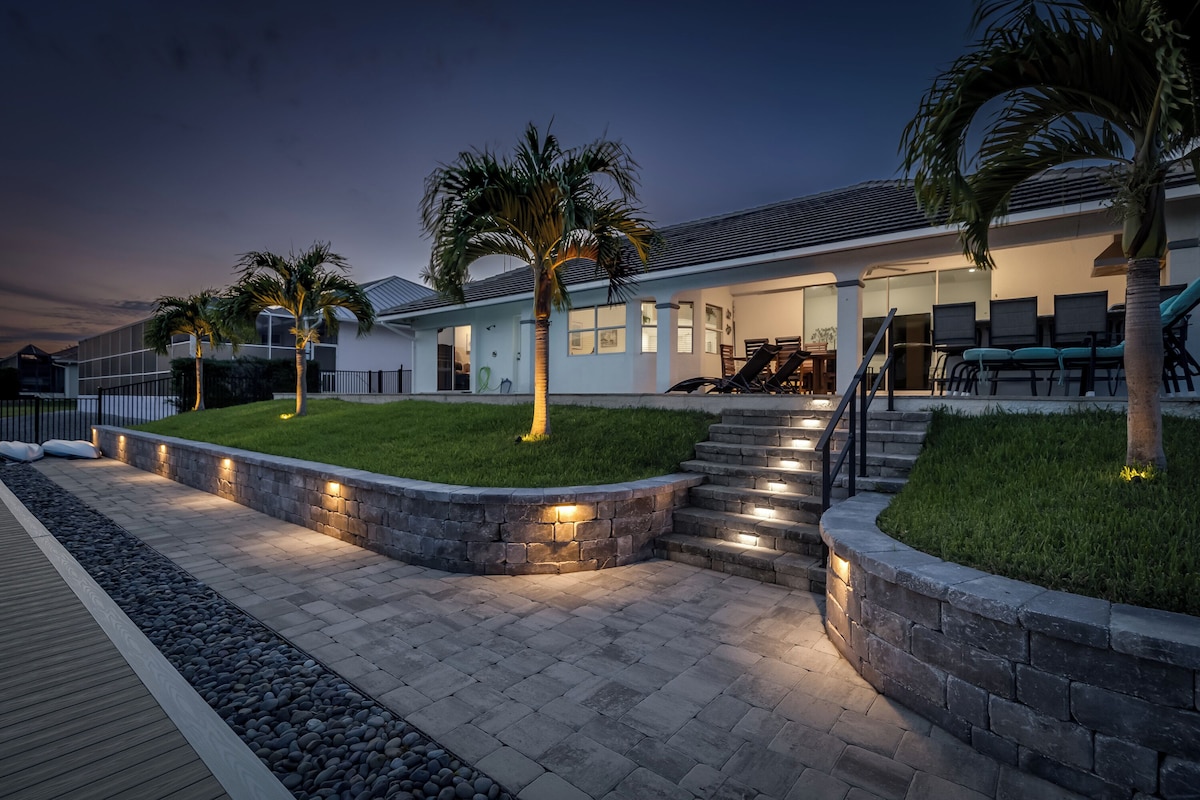 A modern property exterior features illuminated landscaping and terraced outdoor areas in a peaceful neighborhood setting at dusk.
