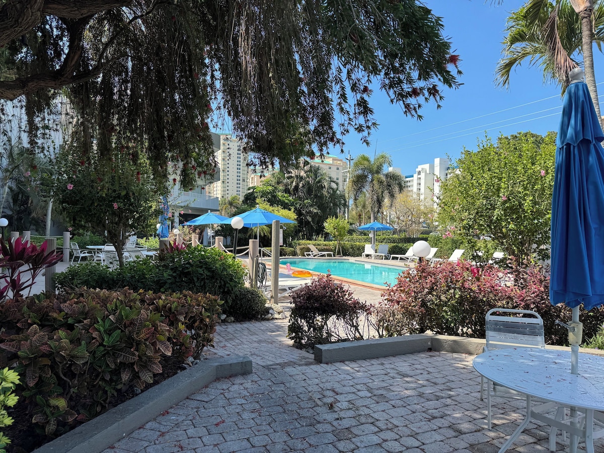 A pool area with lounge chairs, umbrellas, and a clear view of the surrounding buildings.