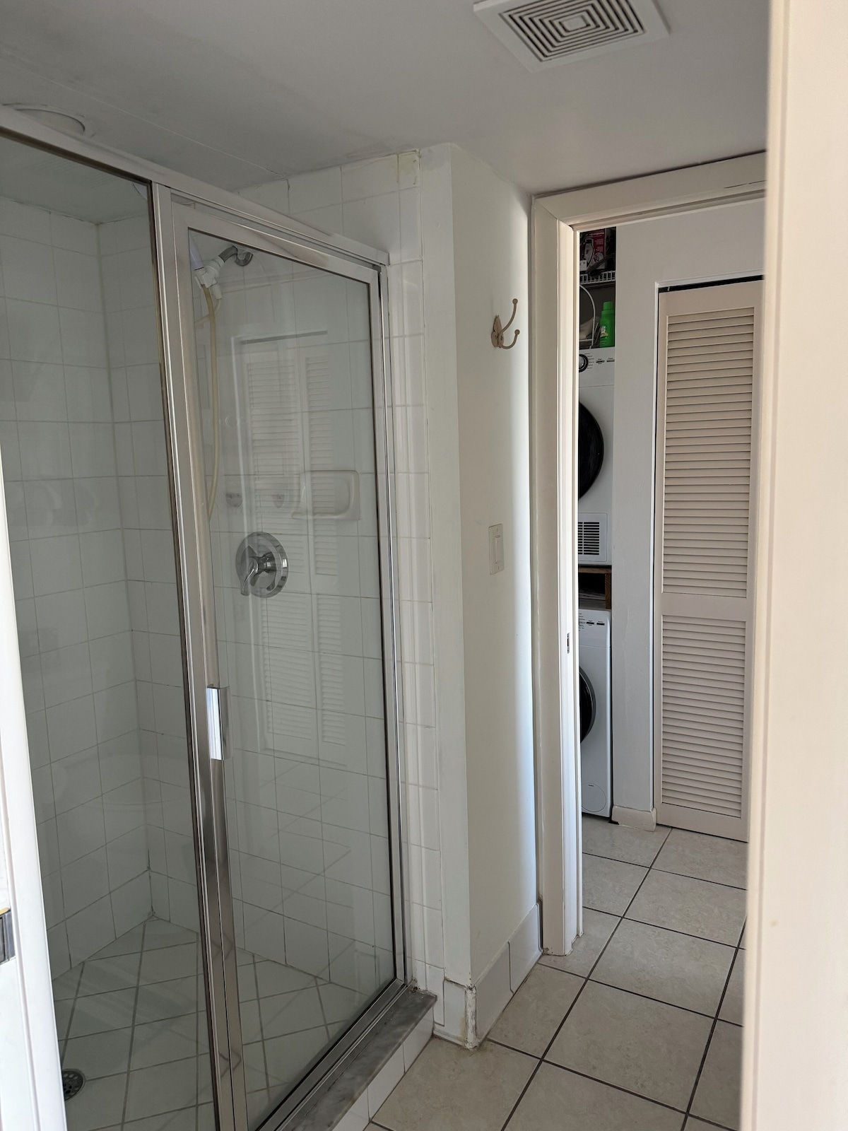 A bathroom with a glass shower enclosure, a tiled floor, and a laundry area with a washing machine and dryer.