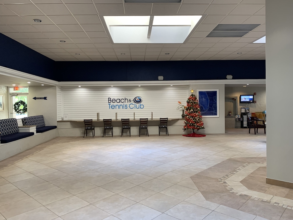 A reception area with a sign for Beach & Tennis Club, a Christmas tree, seating, and a TV screen.