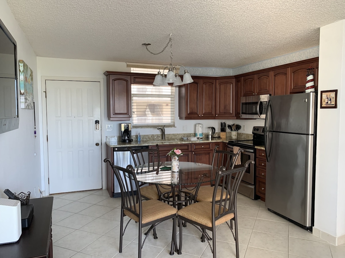 A modern kitchen with dark wooden cabinets, stainless steel appliances, and a dining area with wicker chairs.