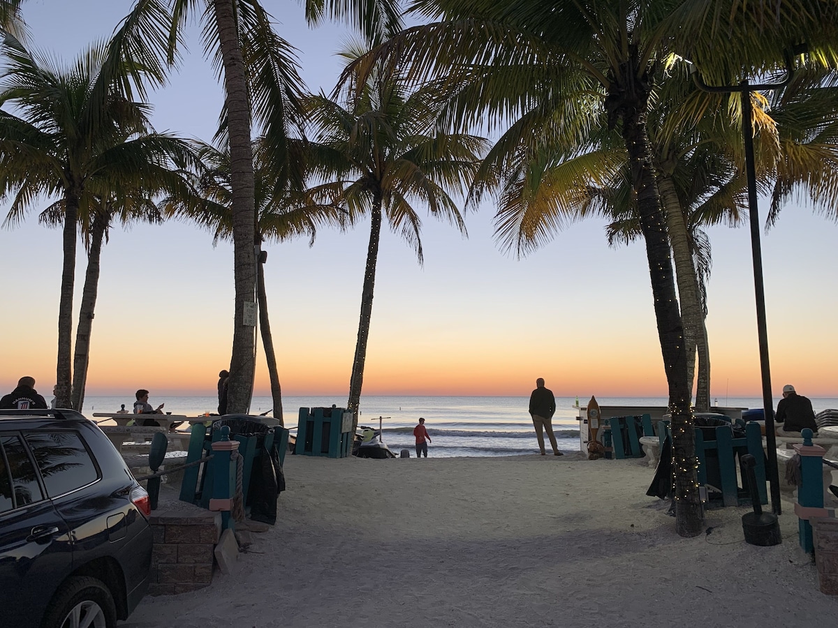 A beach with palm trees, a parked car, and people relaxing.