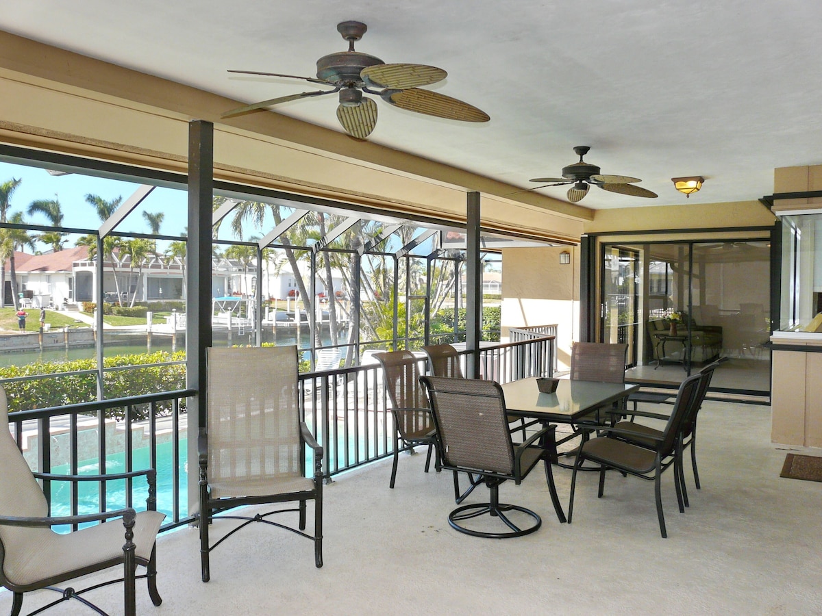A covered outdoor dining area with a pool view, ceiling fans, and a glass railing.