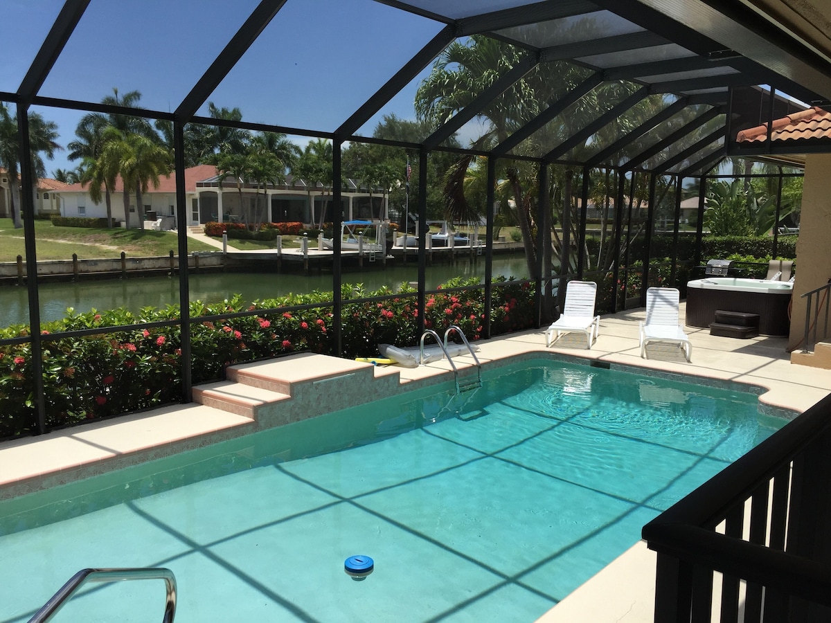 A pool area with a glass enclosure, a hot tub, and a view of a water body and buildings.