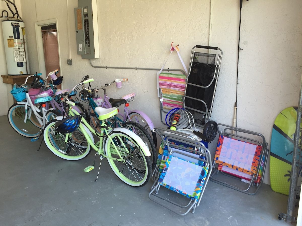 A row of bicycles parked against a wall, a water heater, and a rack with surfboards.