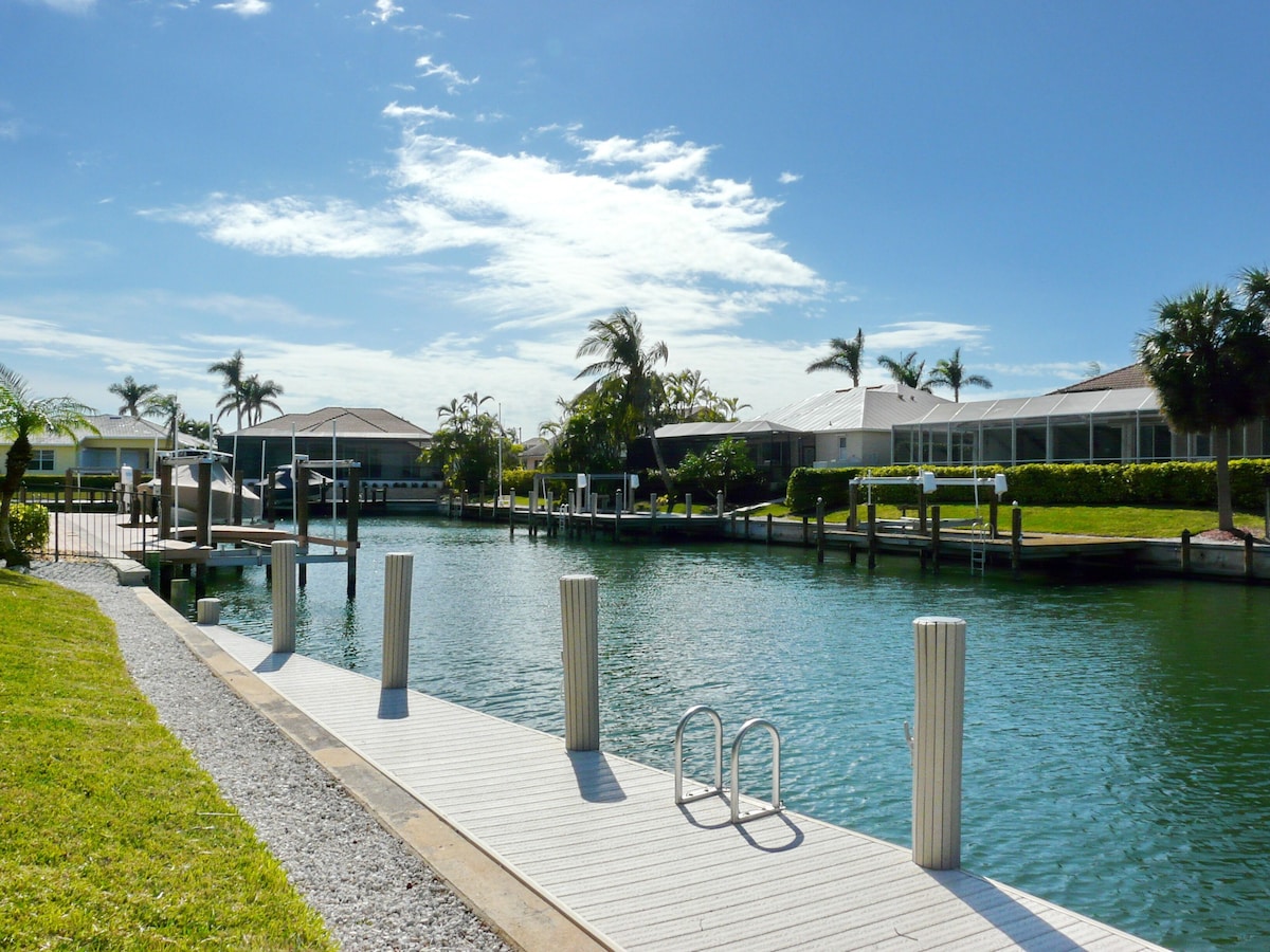A waterfront property with a dock, water, and palm trees.