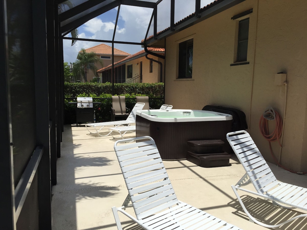 A covered outdoor area with white lounge chairs, a hot tub, and a grill.