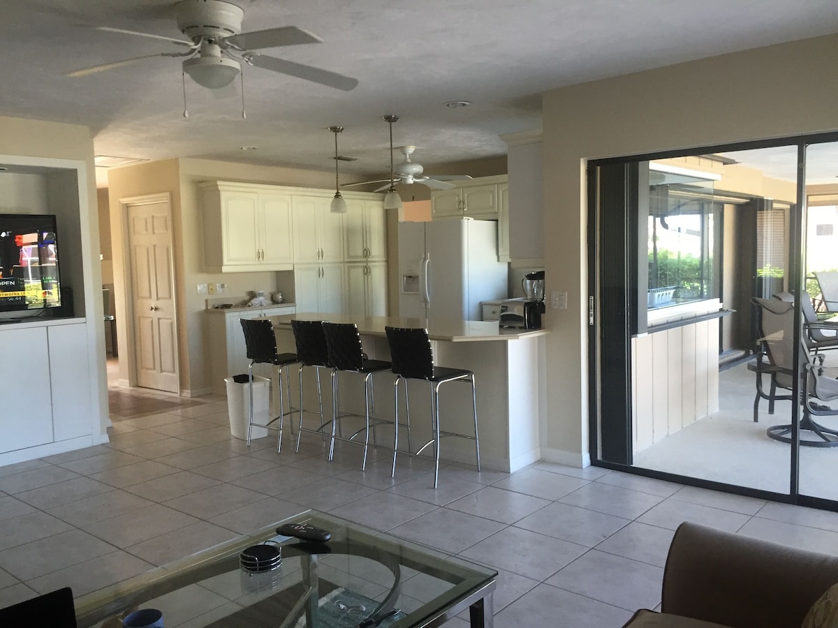 A spacious living area with a glass coffee table, a TV, and a ceiling fan.