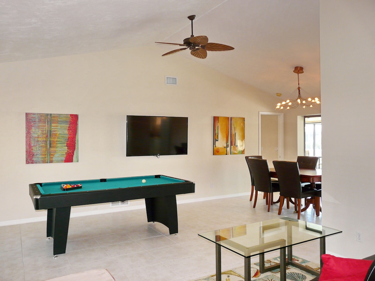 A modern living room with a pool table, a flat-screen TV, and abstract art on the walls.