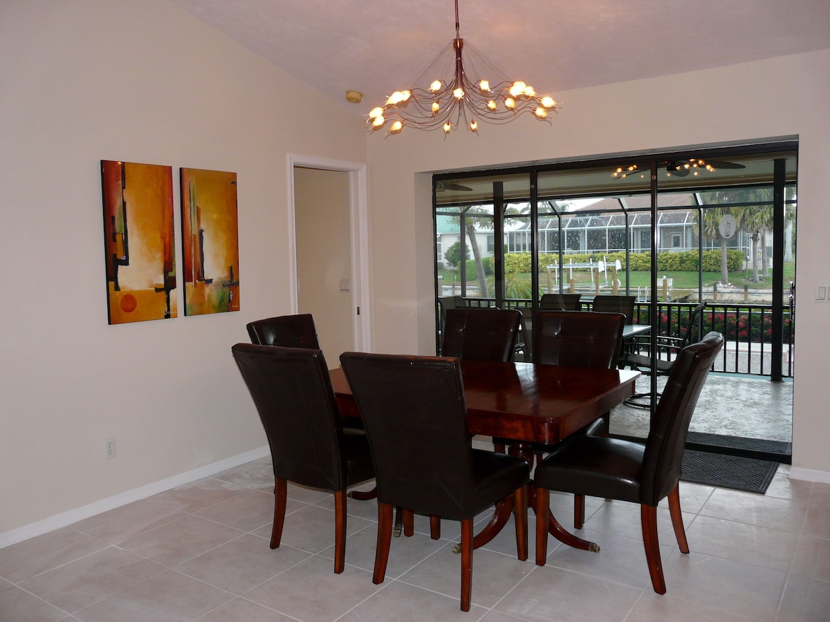 A dining area with a large wooden table and black chairs, a chandelier, and two abstract paintings on the wall.