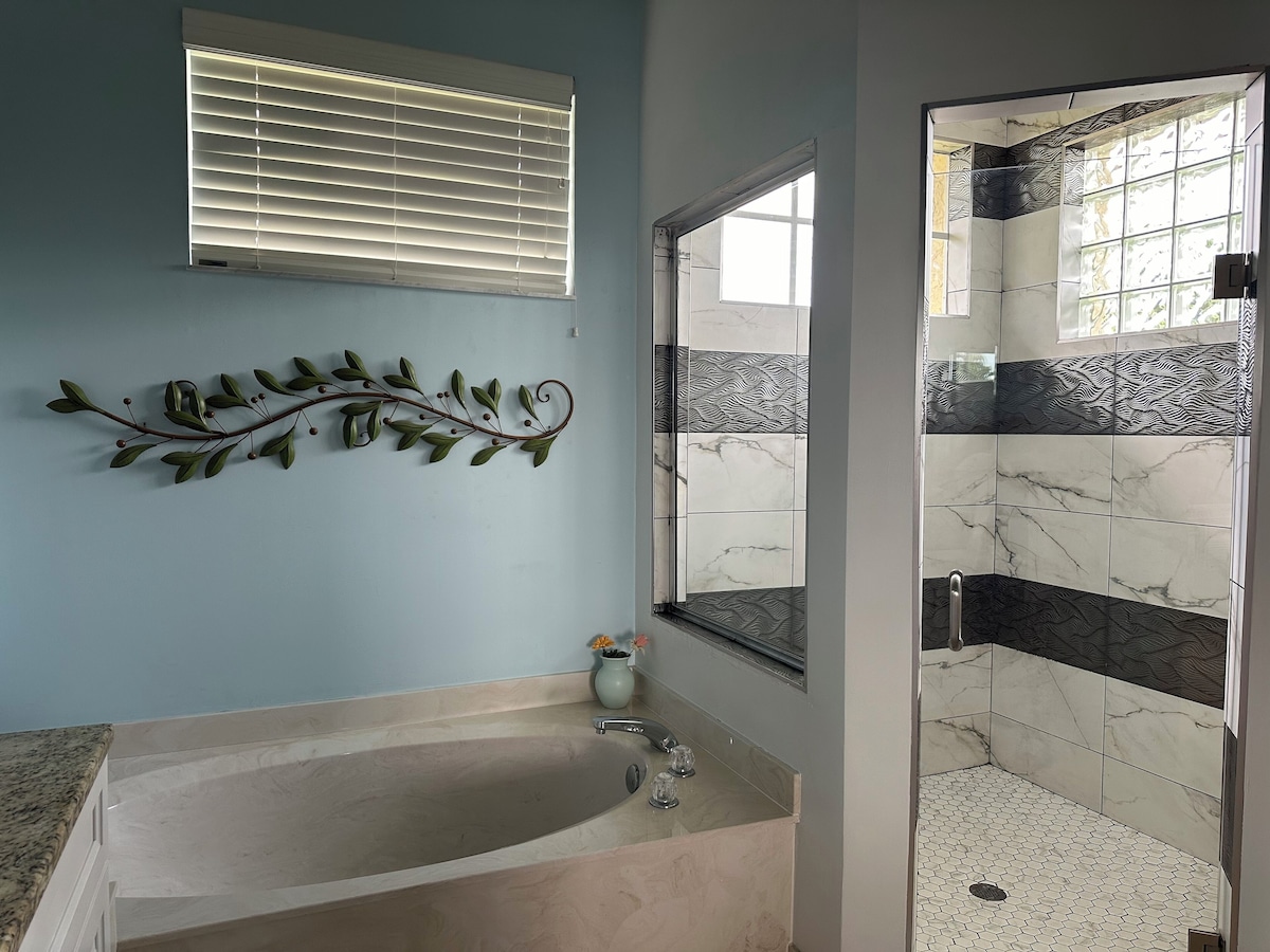 A bathroom with a bathtub, a shower with a tiled wall, and a window with blinds.