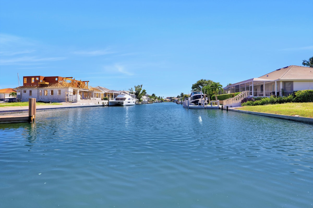 A canal with boats, a house under construction, and another house with a covered porch.