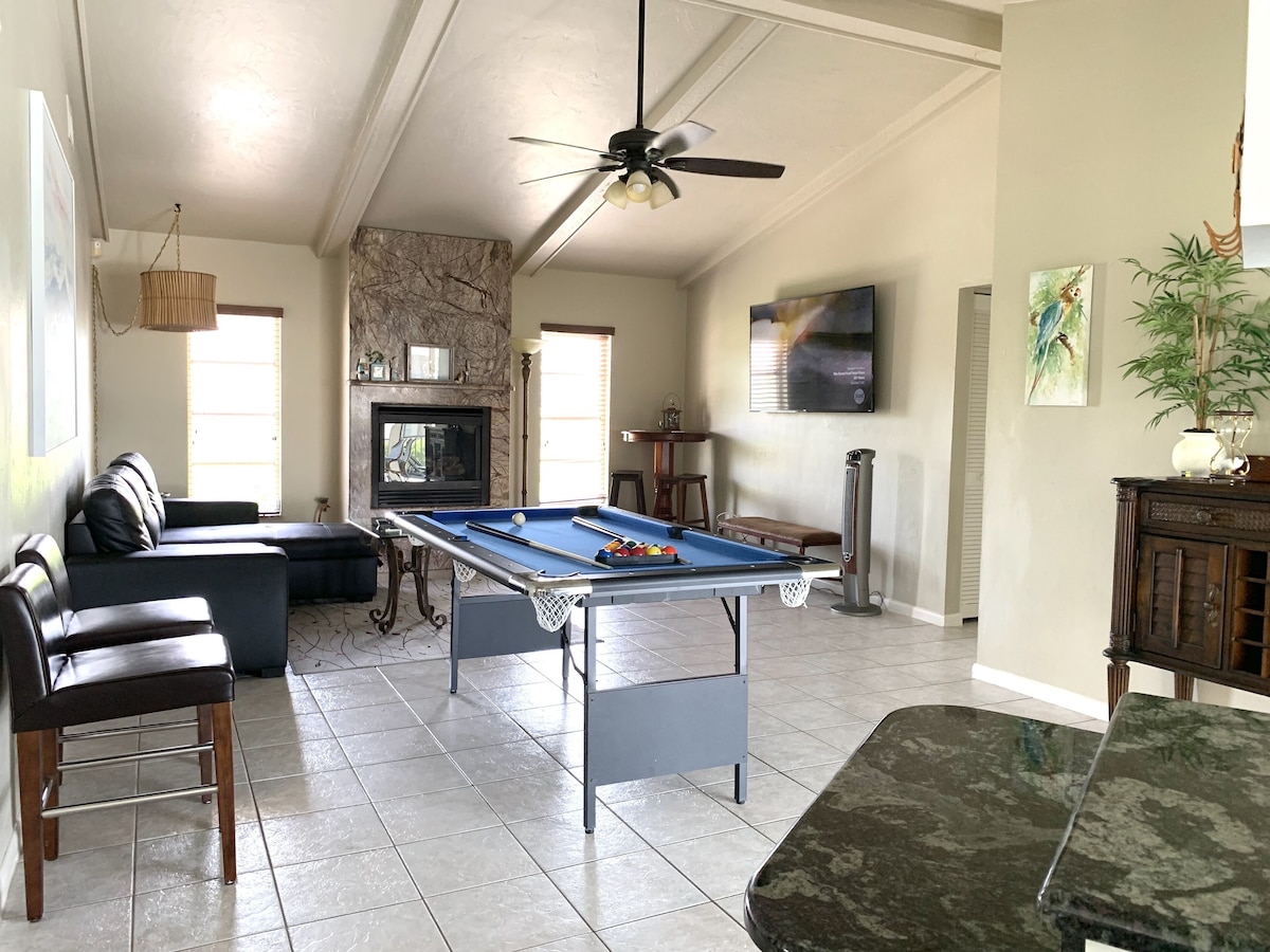 A living room with a pool table, a sofa, a television, and a fireplace.