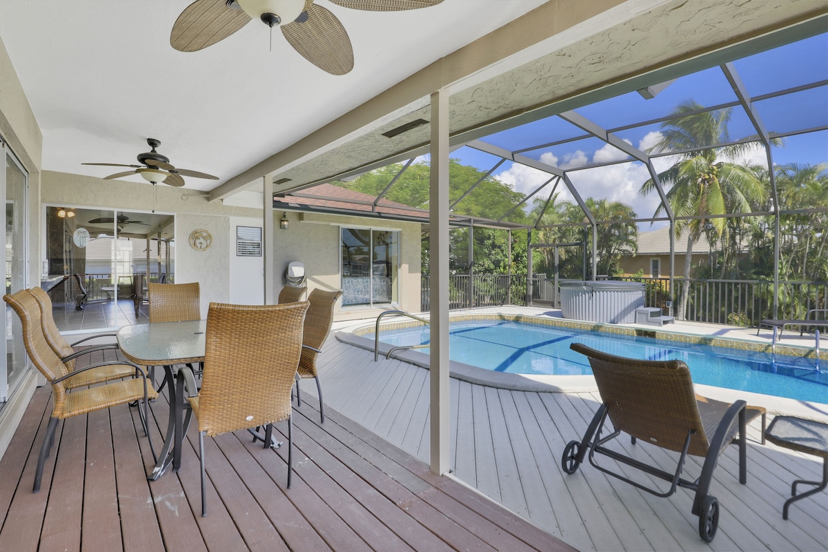 A poolside area with wicker furniture, a glass-enclosed pool, and a view of palm trees.