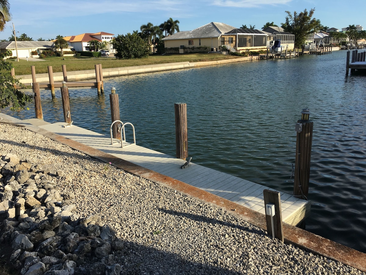 A waterfront property with a dock, a grassy area, and houses in the background.