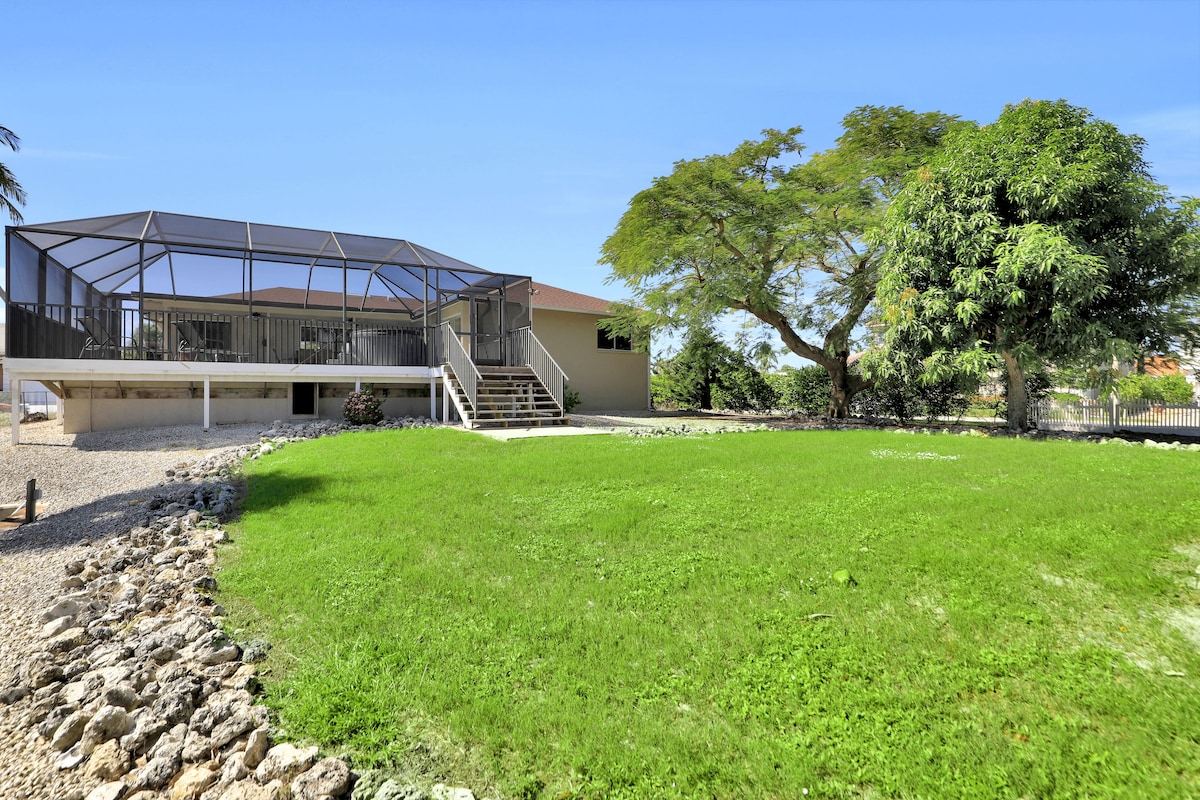 A modern house with a covered patio, a stone pathway, and a large tree in the yard.