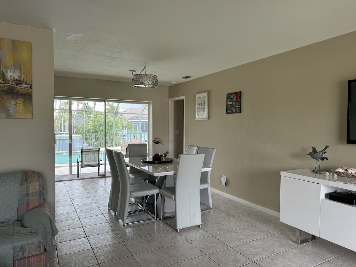 A modern living room with a dining area, a pool view, and a white cabinet with decorative items.
