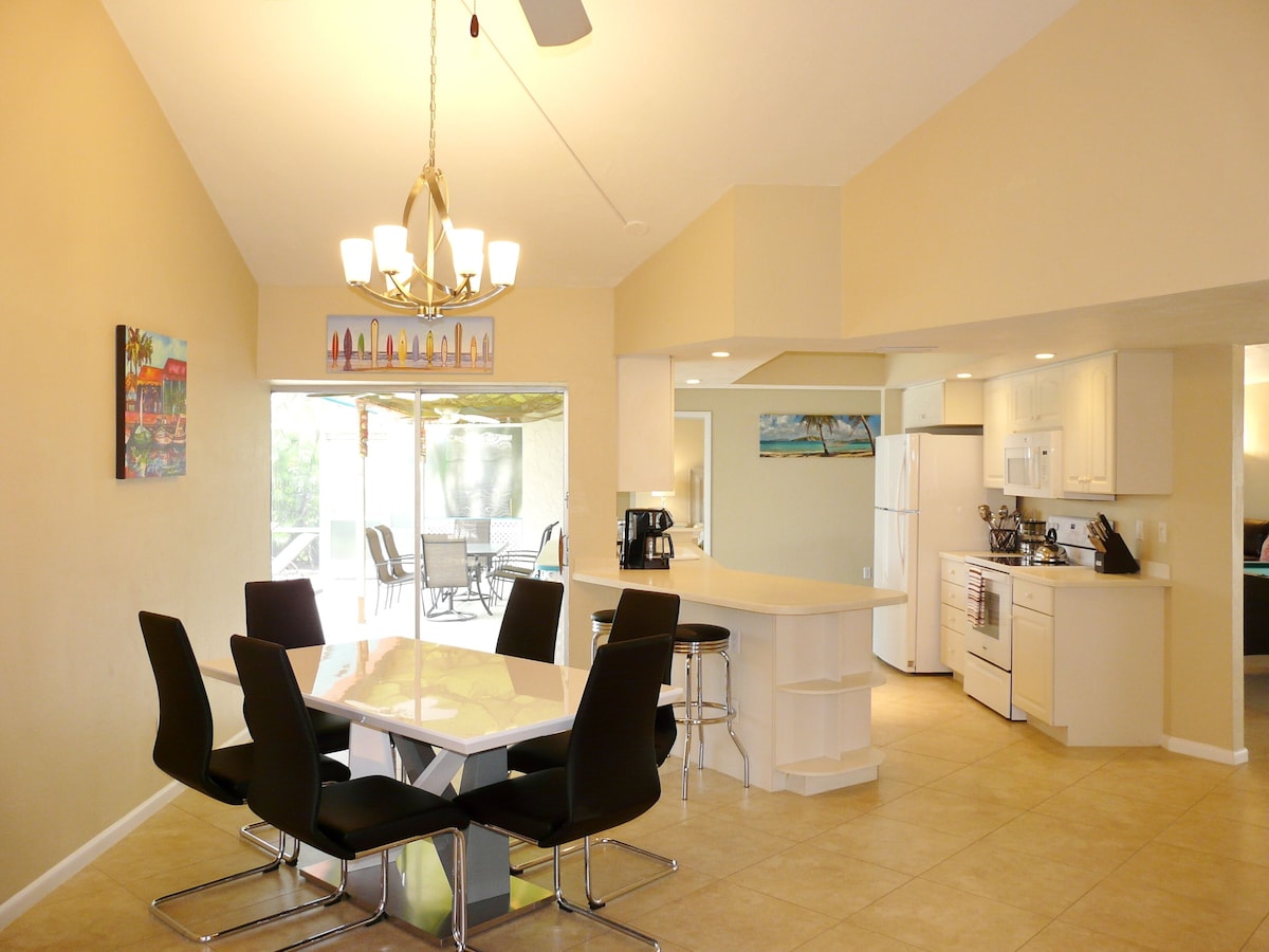 A modern kitchen with white cabinets, a central island, and a dining area with a glass table and black chairs.