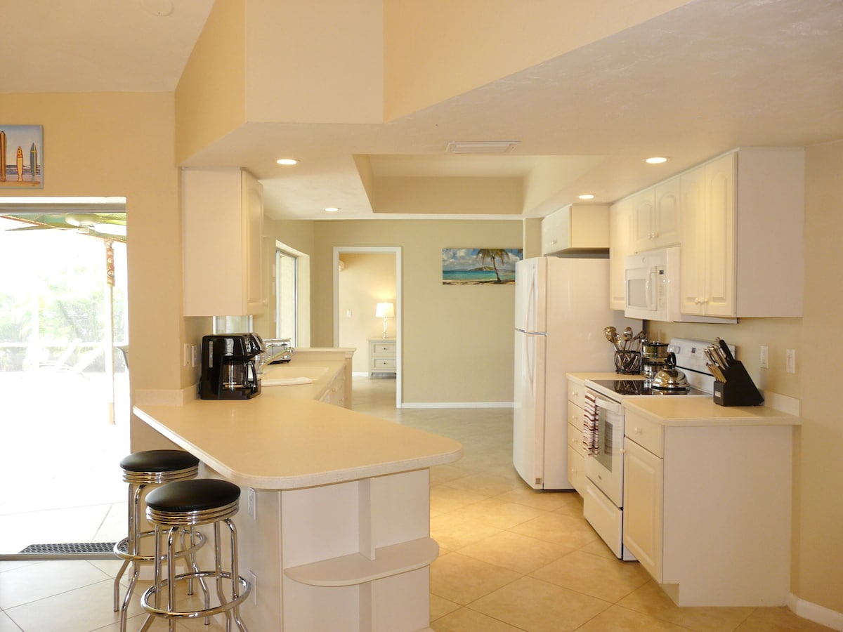 A modern kitchen with white cabinets, a central island with bar stools, a refrigerator, and a microwave.