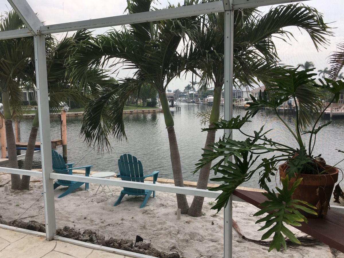 A covered outdoor area with a view of a body of water, palm trees, and blue chairs.