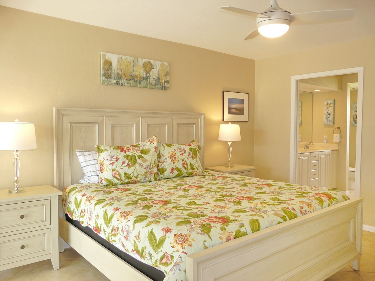 A bedroom with a bed, two nightstands, a ceiling fan, and a bathroom visible through an open door.