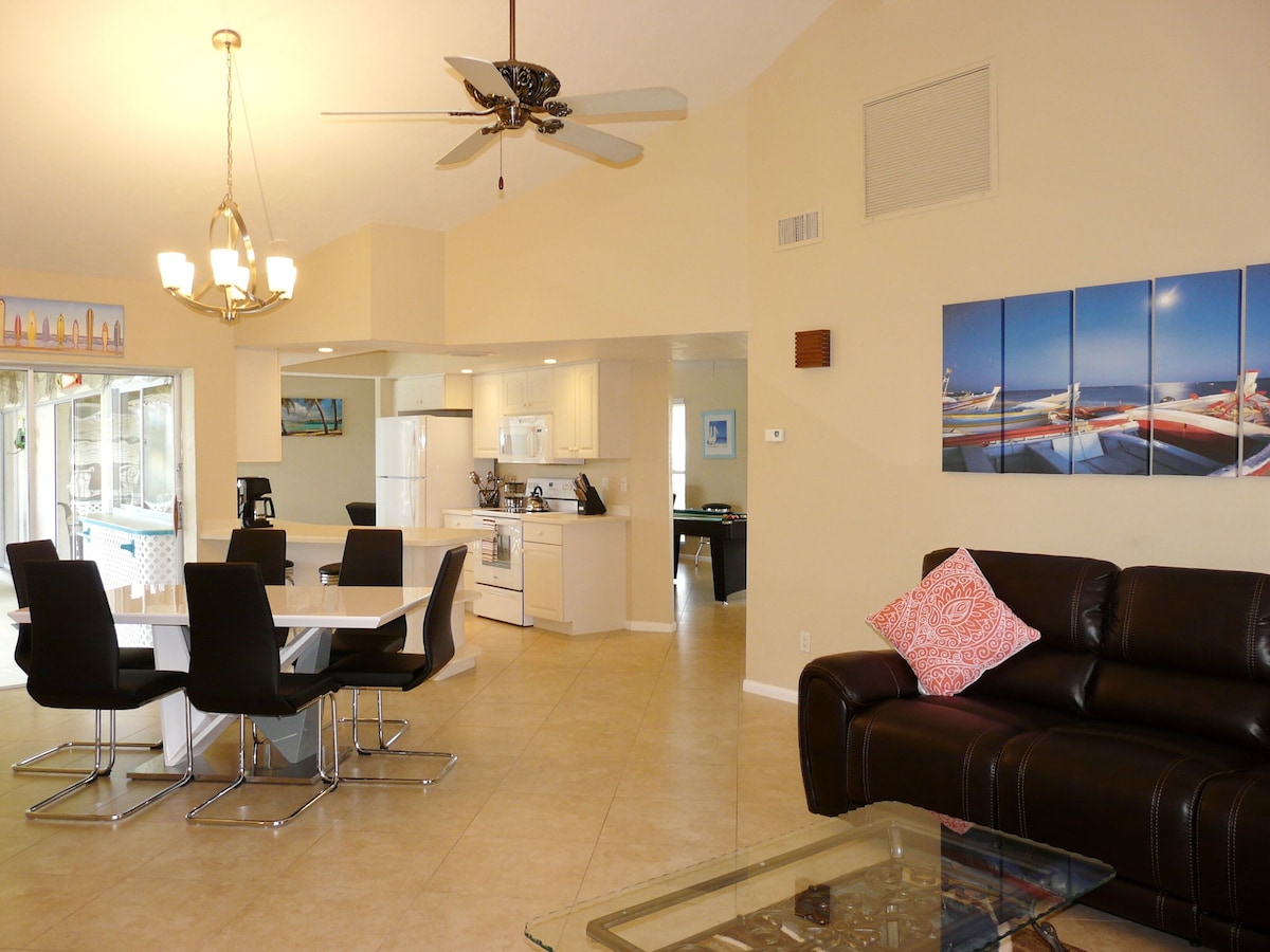 A modern living room with a brown leather couch, a glass coffee table, and a dining area with a white table and black chairs.