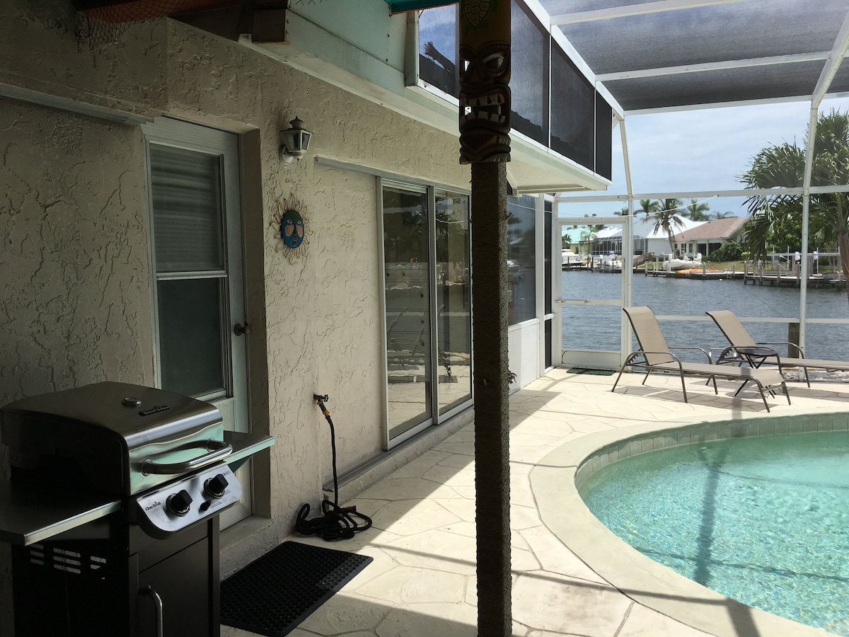 A poolside area with a grill, lounge chairs, and a view of the water.