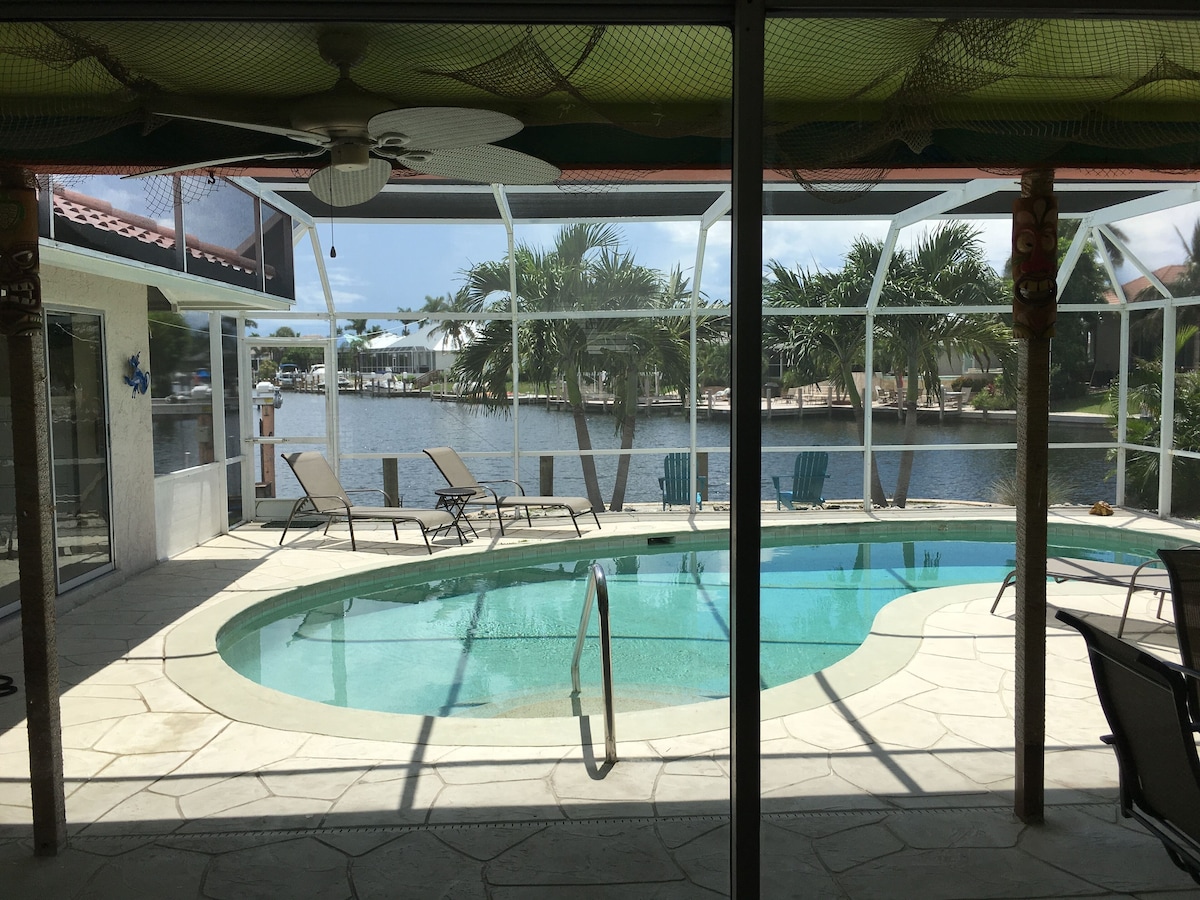 An indoor swimming pool with clear views of a waterfront and palm trees.
