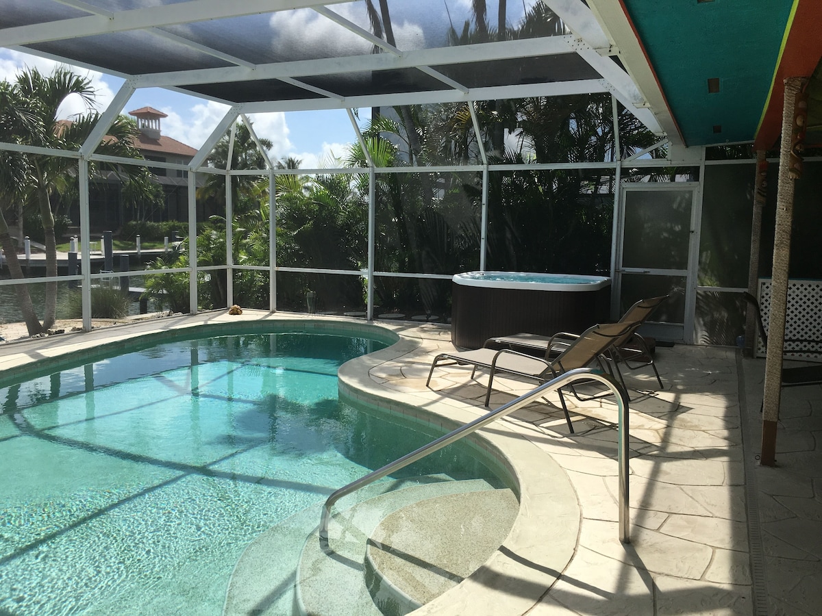 A swimming pool with a hot tub, lounge chairs, and a covered patio area.