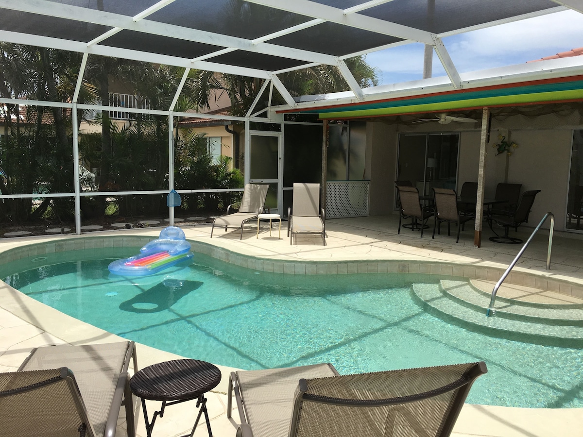A covered outdoor swimming pool with lounge chairs and a table, surrounded by a glass enclosure.
